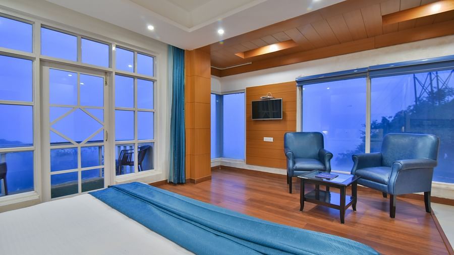 View from the bed of two comfortable chairs next to TV in Luxury Room with Balcony at DLS Highland Resort and Spa, Mussoorie.